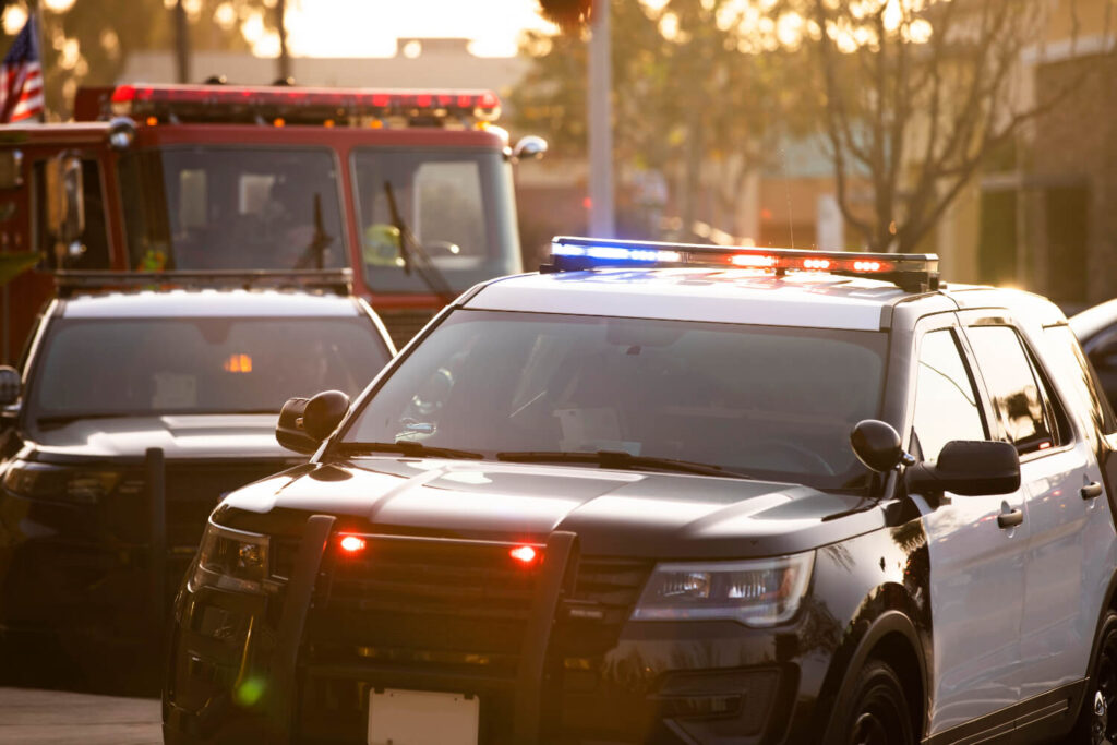 Emergency response scene featuring a police SUV with flashing lights in the foreground and a fire truck in the background.