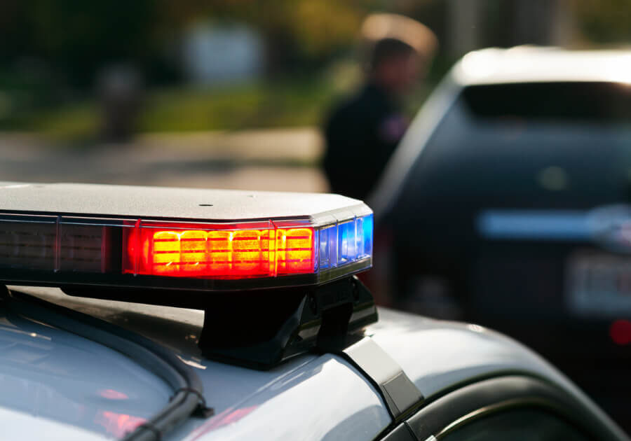 focused view of a police car light while a blurred background shows an officer speaking with a car driver